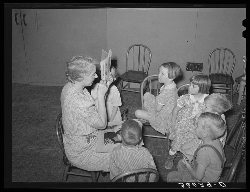 WPA (Work Projects Administration) nursery teacher telling and showing picture story to children of agricultural workers at…