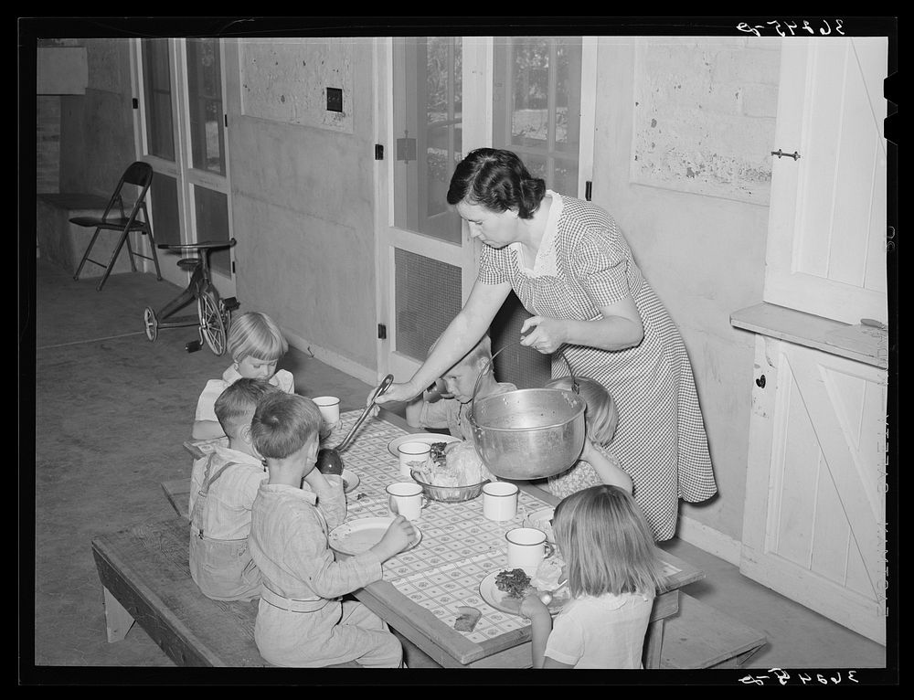 WPA (Work Projects Administration) nursery school supervisor "helping the plates" of the children who have their lunches at…