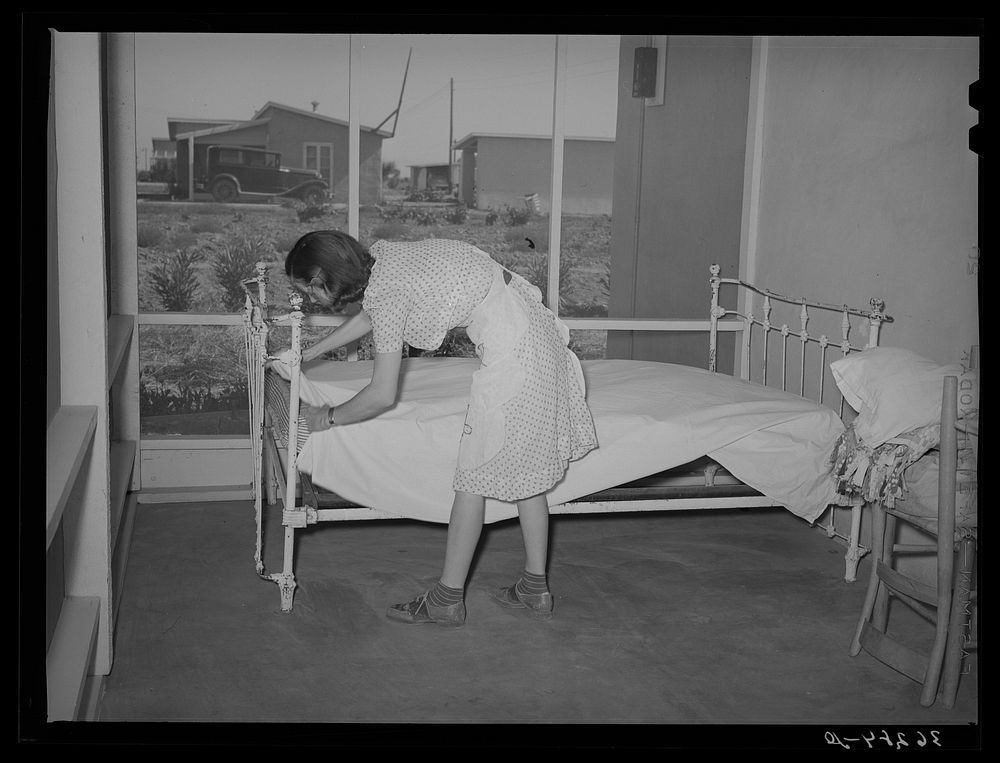 Wife of member of the Casa Grande Valley Farms, Pinal County, Arizona making up bed on her porch. These large porches on all…