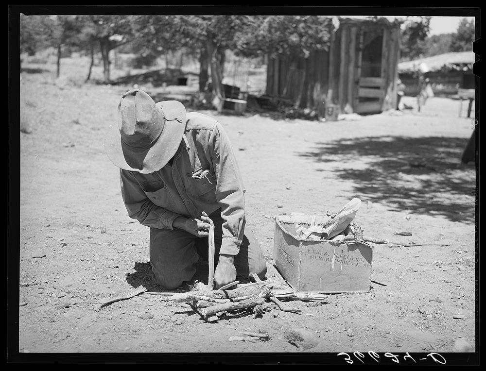 [Untitled photo, possibly related to: Faro Caudill building a fire to cook dinner while he moves his dugout. Pie Town, New…