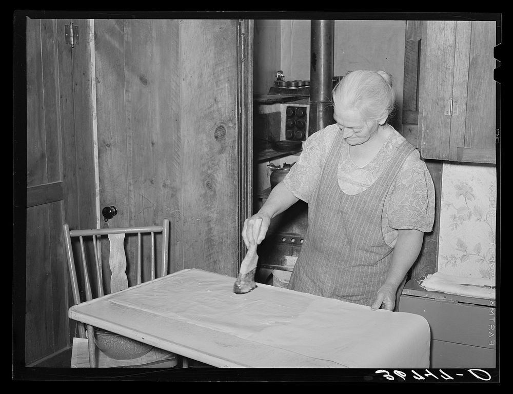 Mrs. George Hutton brushing on paste on wall paper which her son is hanging for her. Pie Town, New Mexico by Russell Lee