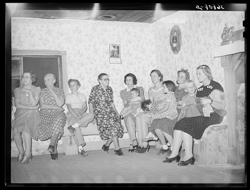Spectators at the square dance. Women and small children sit on one side of the room, the men and older boys on the other.…