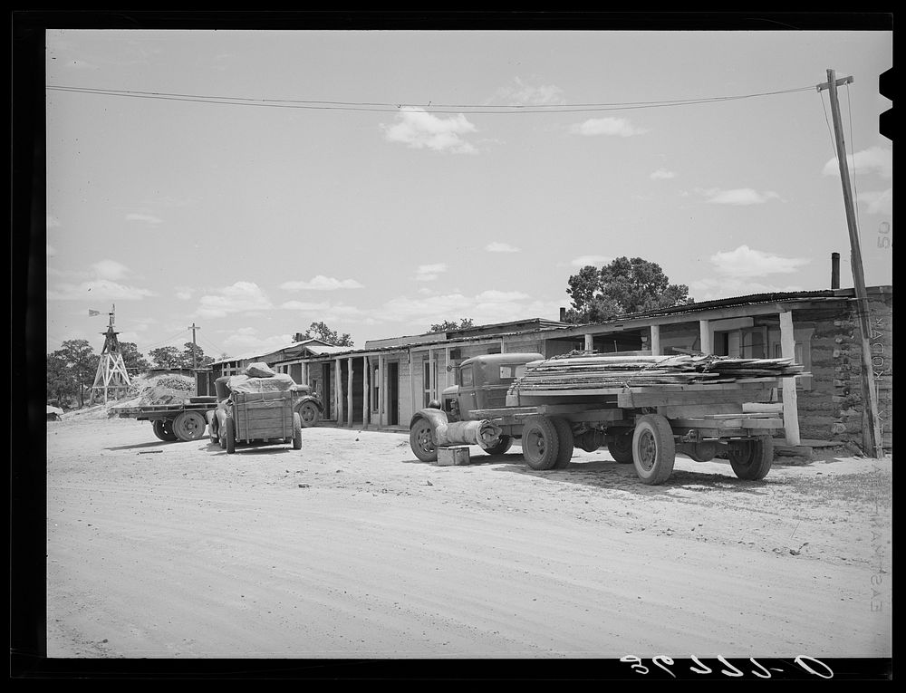 Trucks from a small sawmill stand in front of the cabins at Pie Town, New Mexico by Russell Lee