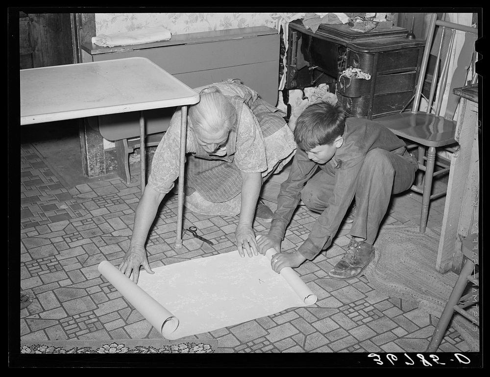 Mrs. Hutton and her grandson unrolling wallpaper for the kitchen. Pie Town, New Mexico by Russell Lee