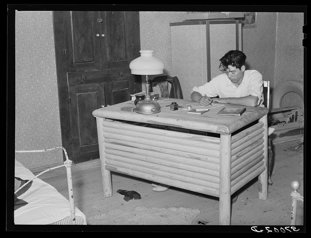 Spanish-American boy working at desk which he made. Notice the similarity in the design of the desk to that of the vigas in…