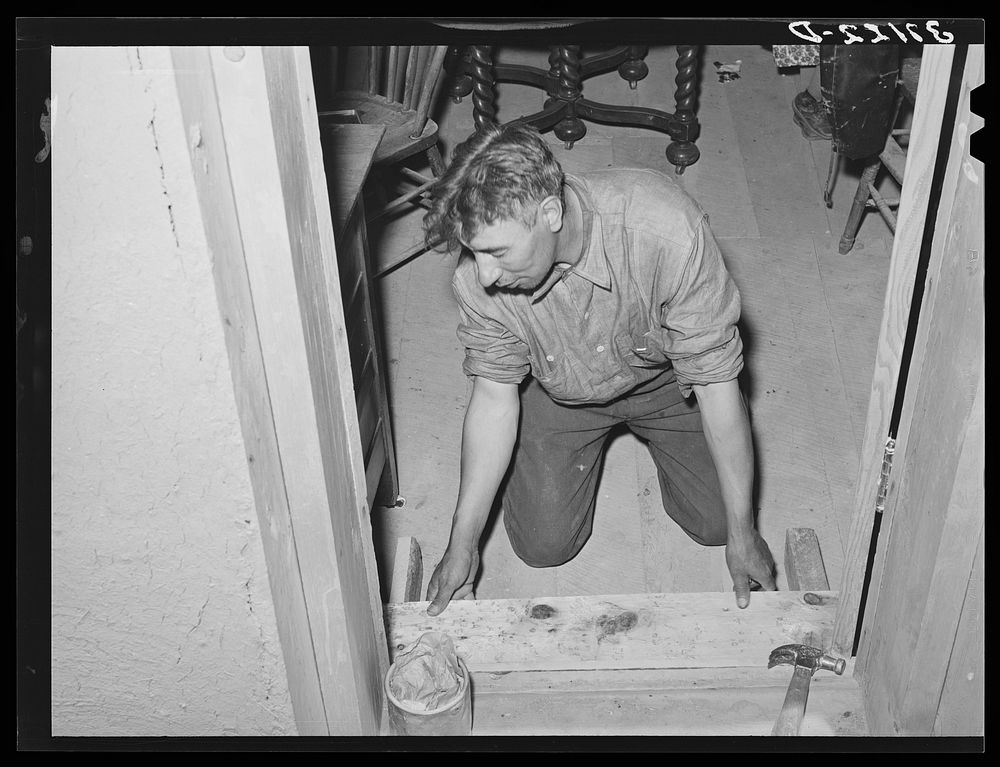 Spanish-American farmer fitting floor step into place. Amalia, New Mexico.  The Spanish-Americans are adept in carpentry and…