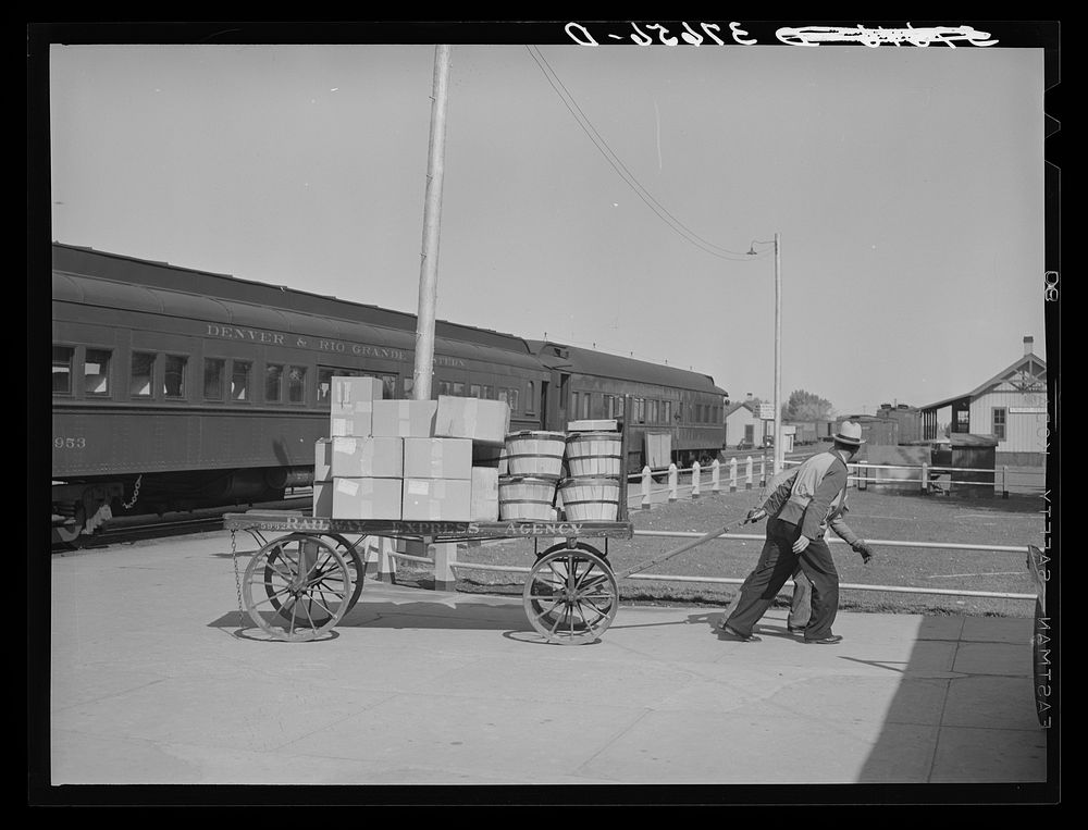 Pulling carload of express packages away from train immediately after the arrival of the morning train. Montrose, Colorado…
