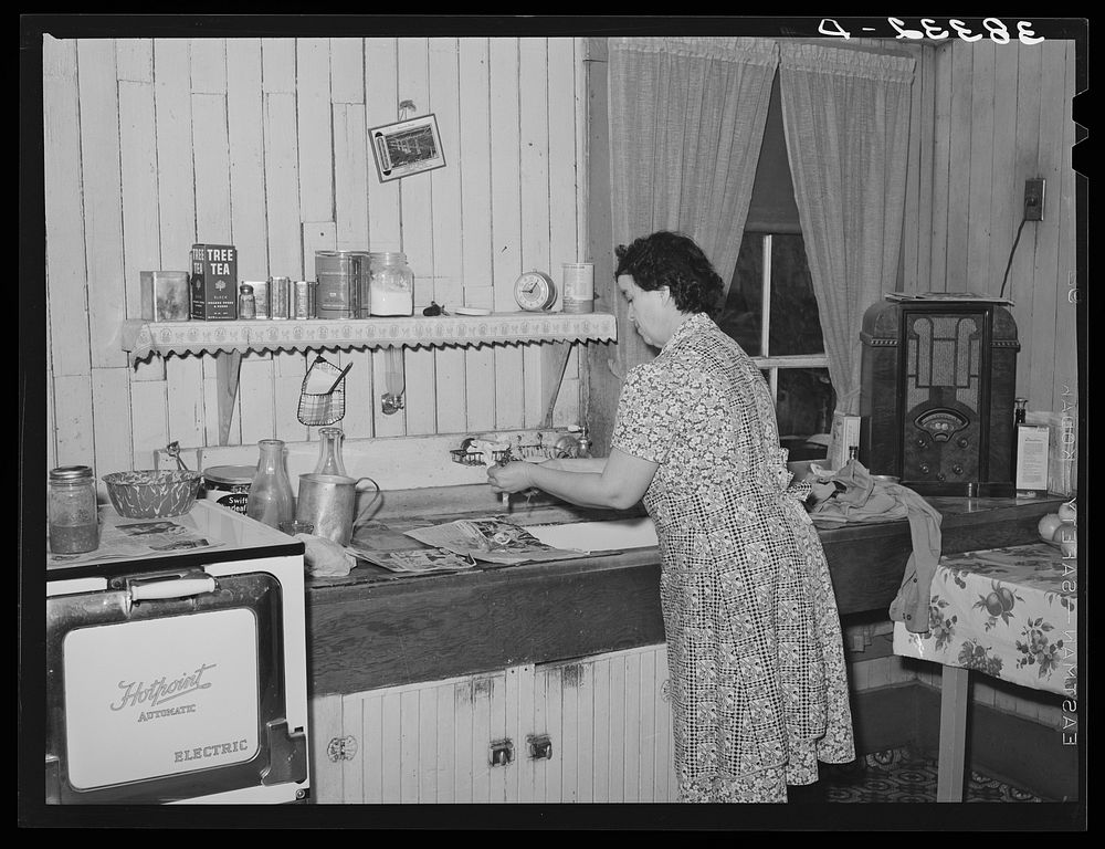 Wife of farmer in her kitchen. Auburn, California. Notice the electric stove, running water and radio. Electrification has…