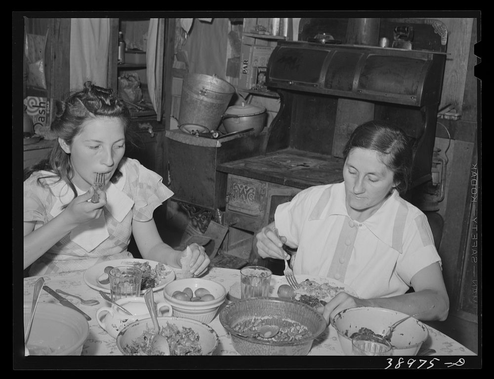 Mrs. Browning and her daughter eating dinner. This family does much canning in line with FSA (Farm Security Administration)…