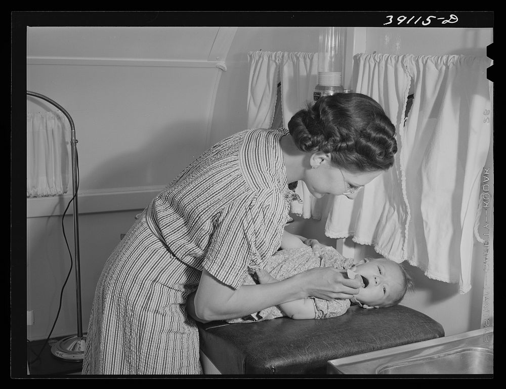 Nurse at the FSA (Farm Security Administration) migratory labor camp mobile unit, examines throat of baby in trailer-clinic.…