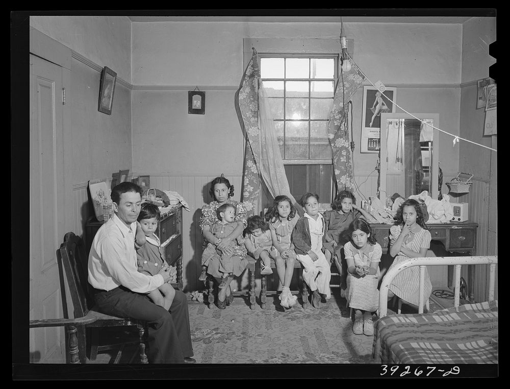 Family group in interior of house in Mexican section. This man is an agricultural worker. This family of two adults and…