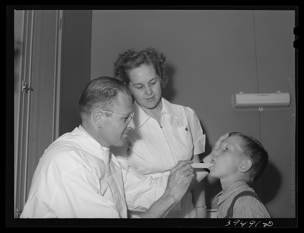 Doctor and nurse with son of farm worker at the clinic at the FSA (Farm Security Administration) labor camp, Caldwell, Idaho…