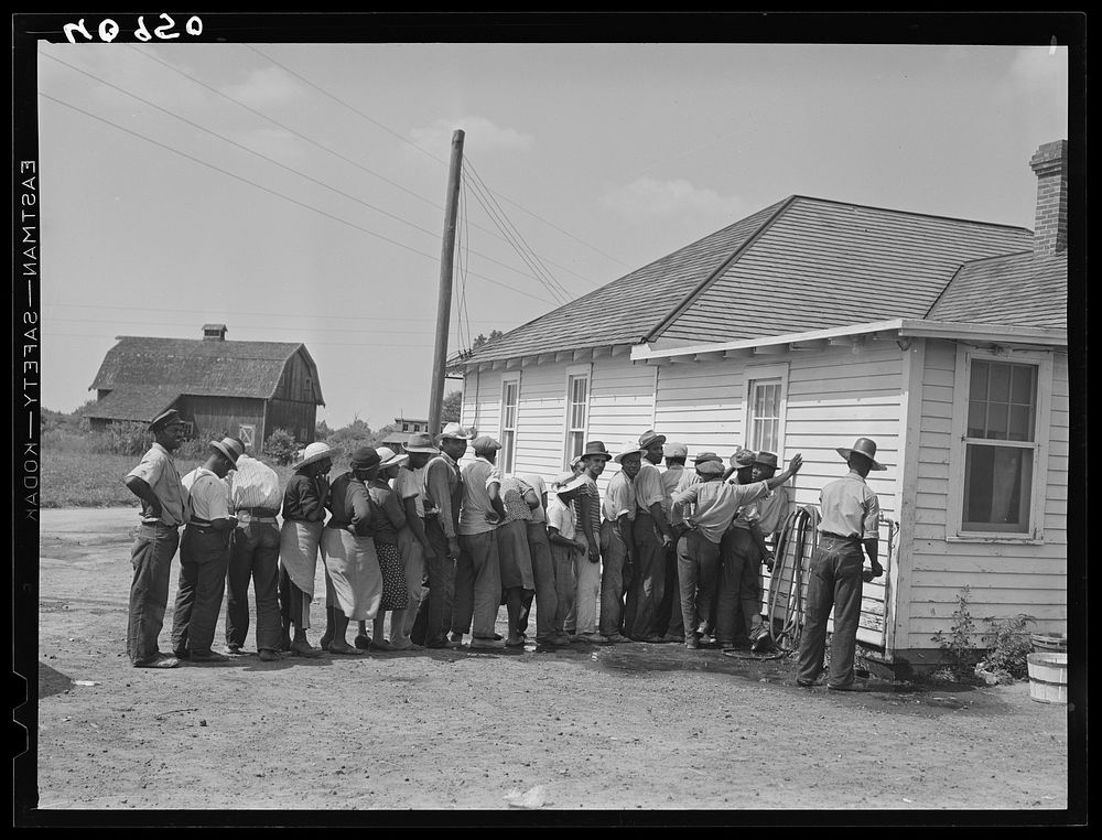 Migratory agricultural workers getting in line to be paid for picking beans. They get seven cents a hundred pounds. Sourced…