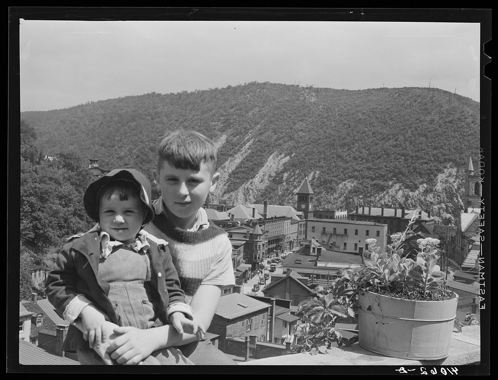 Two children sitting on a stone wall on High Street, Mauch Chunk. The town is below them and Bear Mountain in the…