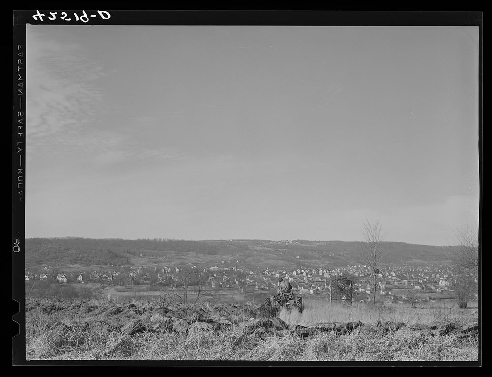 [Untitled photo, possibly related to: Farmer ploughing his field on a hillside opposite the industrial valley including the…