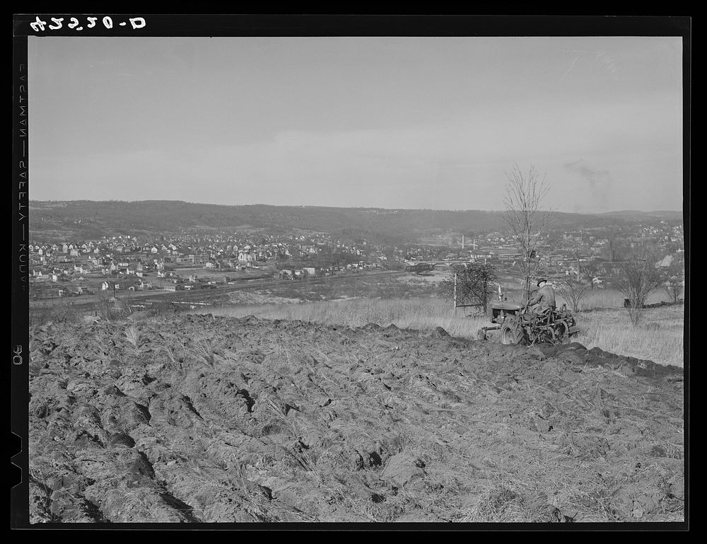 Farmer ploughing his field on a hillside opposite the industrial valley including the towns of Darby, Shelton, and Ansonia…