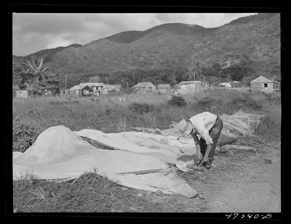 French village, a small settlement on Saint Thomas Island, Virgin Islands. Fishermen laying out sails to dry on the beach of…