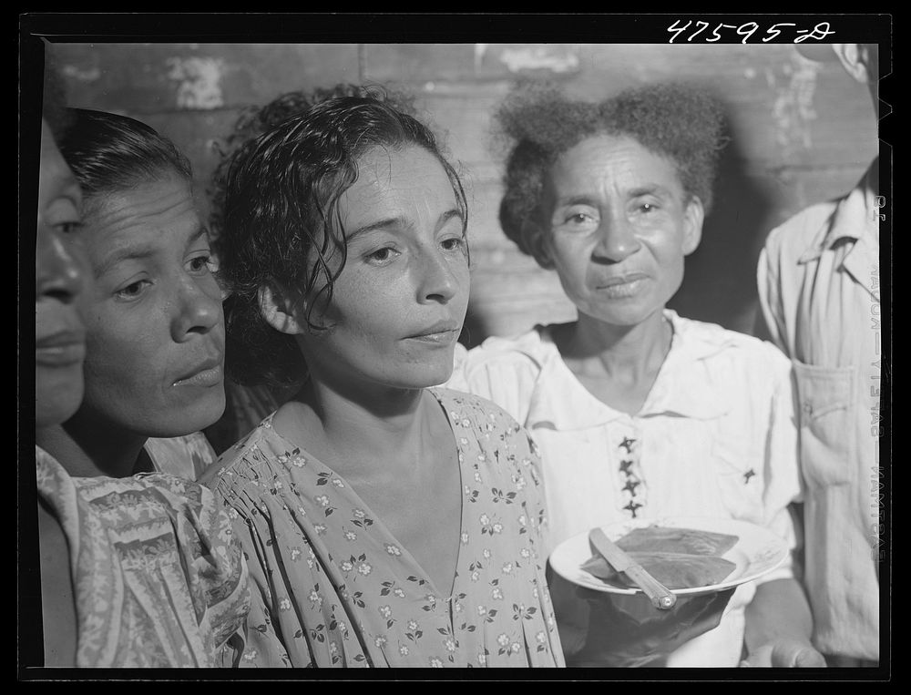 Guanica, Puerto Rico (vicinity). At a Three Kings' eve party in the home of a farm laborer's family. The woman is serving…