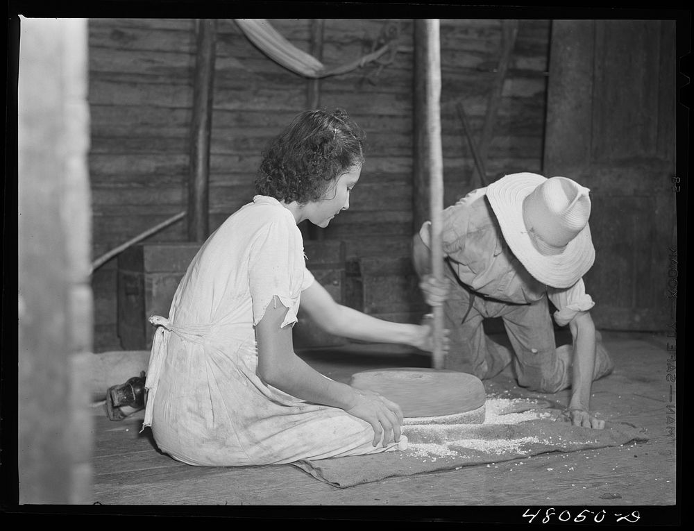 San Sebastian, Puerto Rico (vicinity). Grinding corn with primitive stones in the home of a farm laborer. Sourced from the…