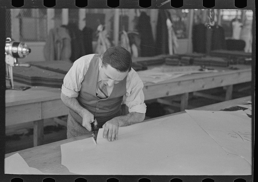 Louis Gushen, chief cutter in the cooperative garment factory of Jersey Homesteads, is cutting the pattern for a woman's…