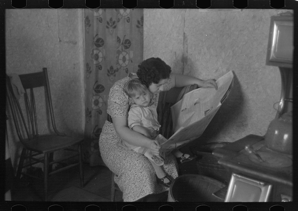 Child on lap of mother reading the newspaper. Nissen shack near Dickens, Iowa by Russell Lee