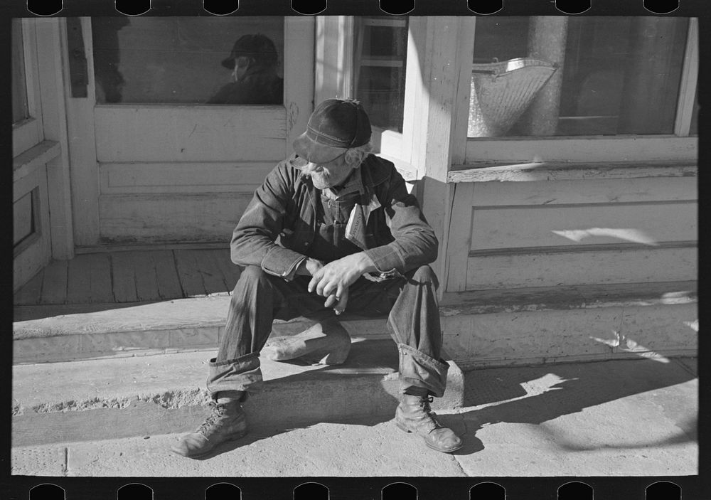 Arnegard, McKenzie County, North Dakota. Old man sitting on a store step by Russell Lee