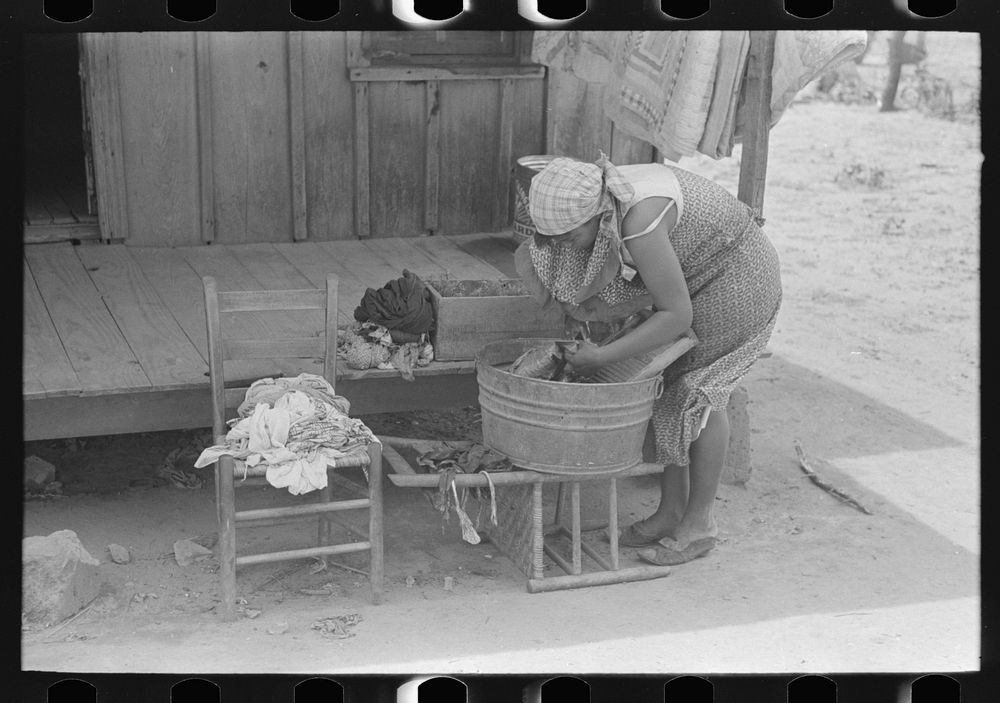Wife of FSA (Farm Security Administration) client, former sharecropper, washing clothes in front of old cabin, Southeast…