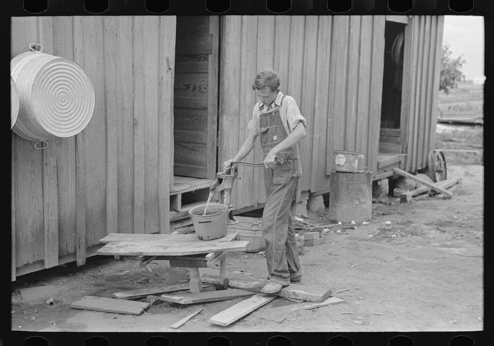 Son of sharecropper pumping water in rear of cabin home, New Madrid County, Missouri by Russell Lee