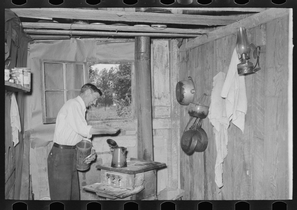 Squatter makes coffee in kitchen at his home in abandoned warehouse, Caruthersville, Missouri by Russell Lee