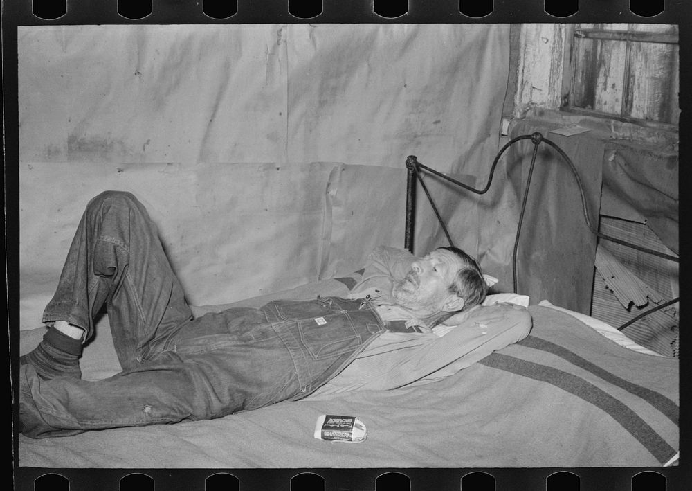 Squatter resting on bed in abandoned warehouse; he was in ill health. Caruthersville, Missouri by Russell Lee