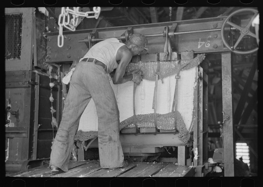 Putting steel straps in place to hold pressed cotton after pressure has been removed, Lehi, Arkansas cotton gin by Russell…
