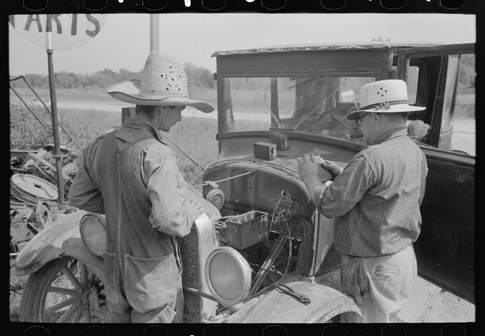 Farmer watching junkyard owner examining condition of spark coils in model-T Ford, Abbeville, Louisiana by Russell Lee