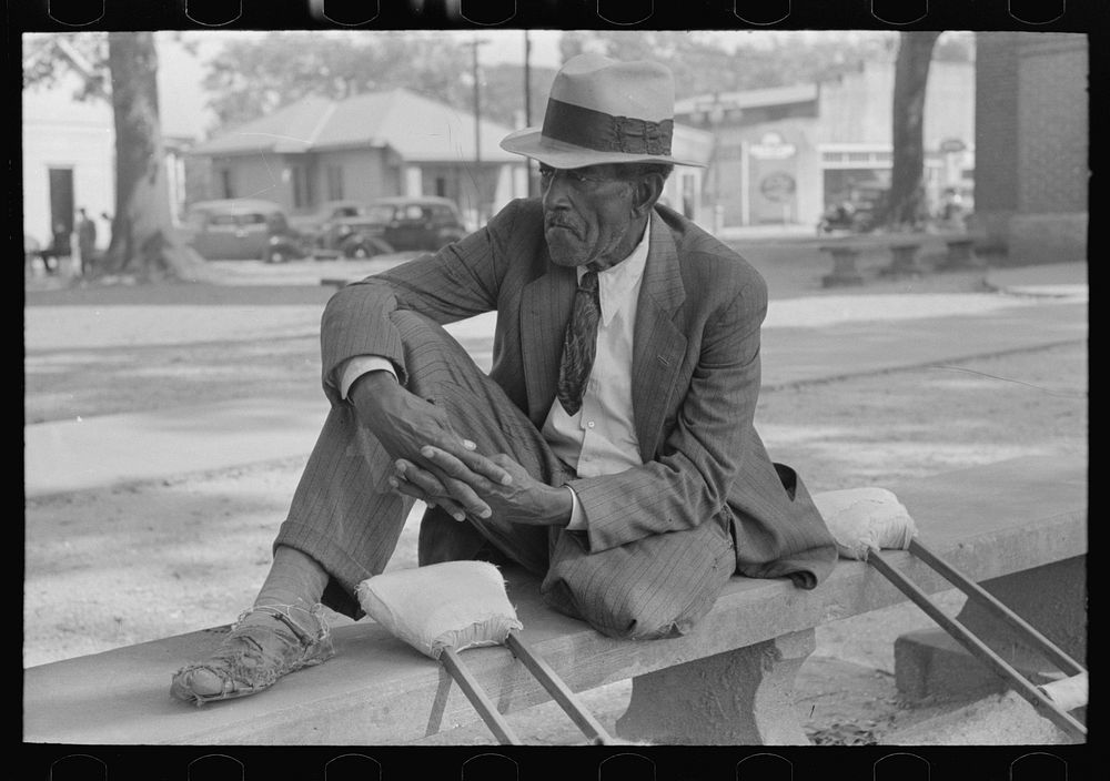 Crippled man sitting on bench in front of courthouse, Abbeville, Louisiana by Russell Lee