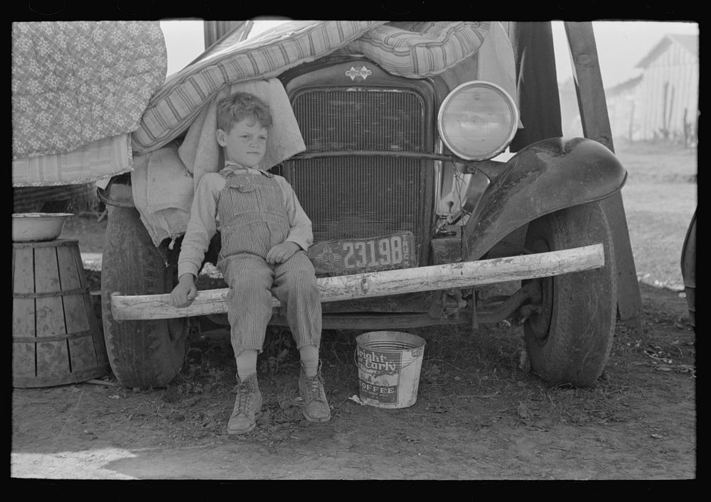 Son of  migrant sitting on bumper of their truck, Weslaco, Texas. Notice New Mexico license by Russell Lee