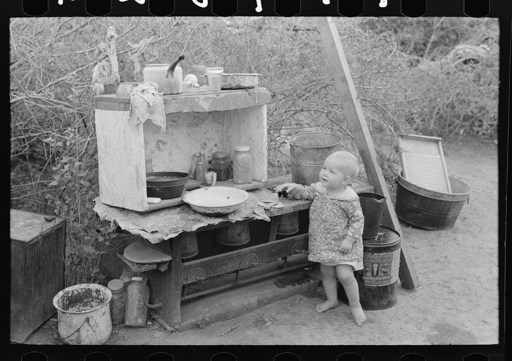 [Untitled photo, possibly related to: Child of migrant worker sitting on bed in tent home of cotton picking sacks…
