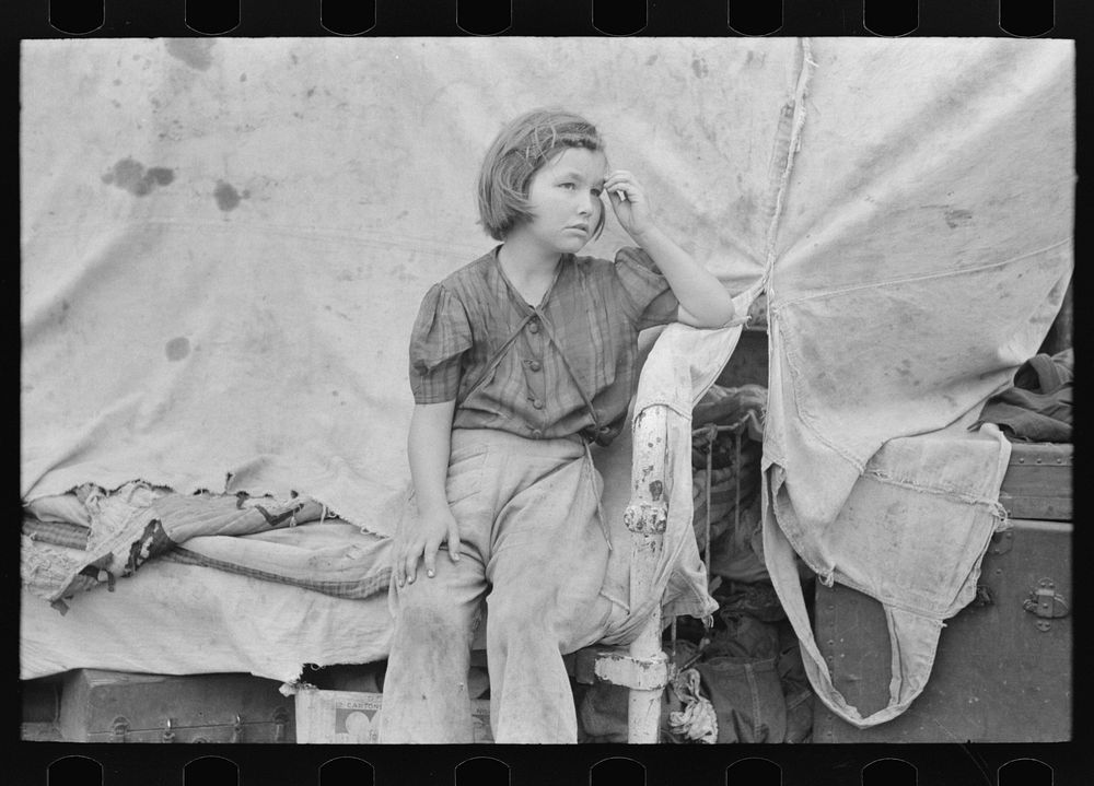 Child of migrant worker sitting on bed in tent home of cotton picking sacks, Harlingen, Texas by Russell Lee