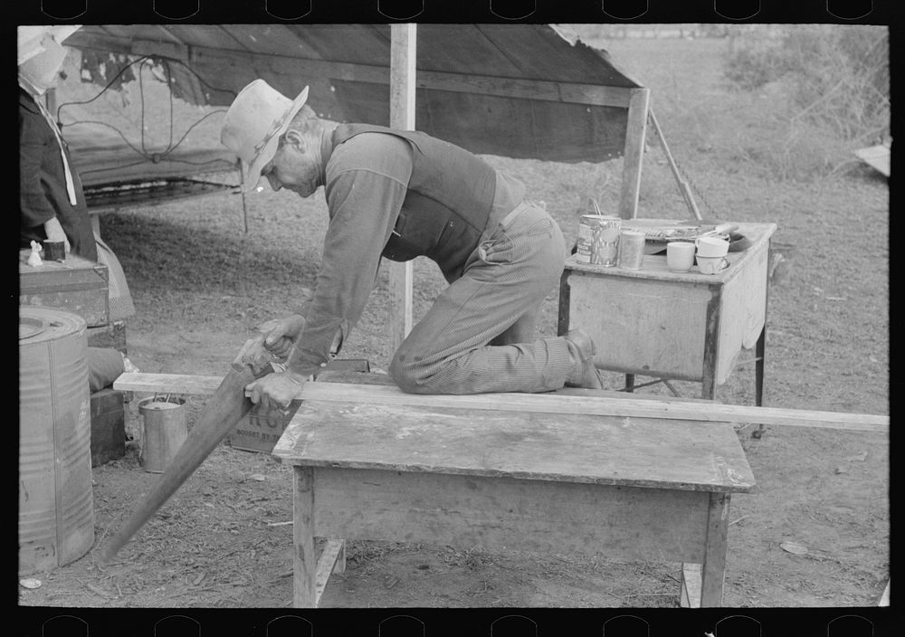 White migrant worker sawing wood for stakes to be used in setting up tent home, near Harlingen, Texas by Russell Lee