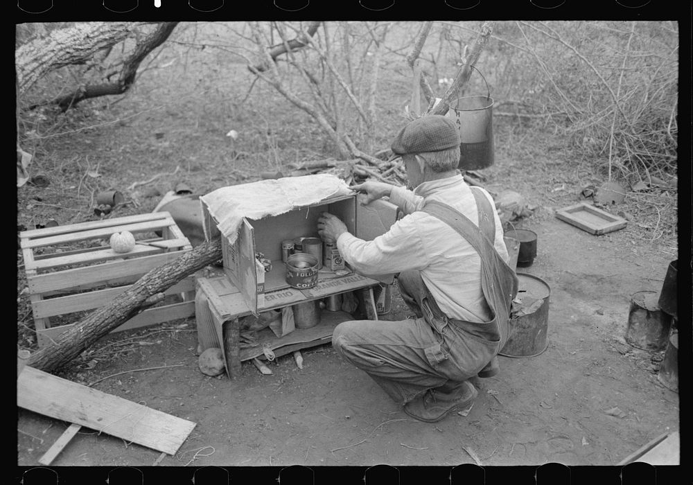 [Untitled photo, possibly related to: White migrant worker living in camp with two other men, working on lean-to which is to…