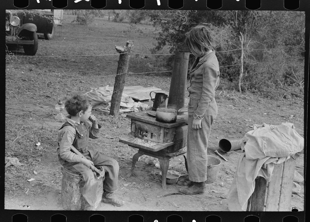 [Untitled photo, possibly related to: Child of white migrant adding water to boiling beans on stove which was set up…