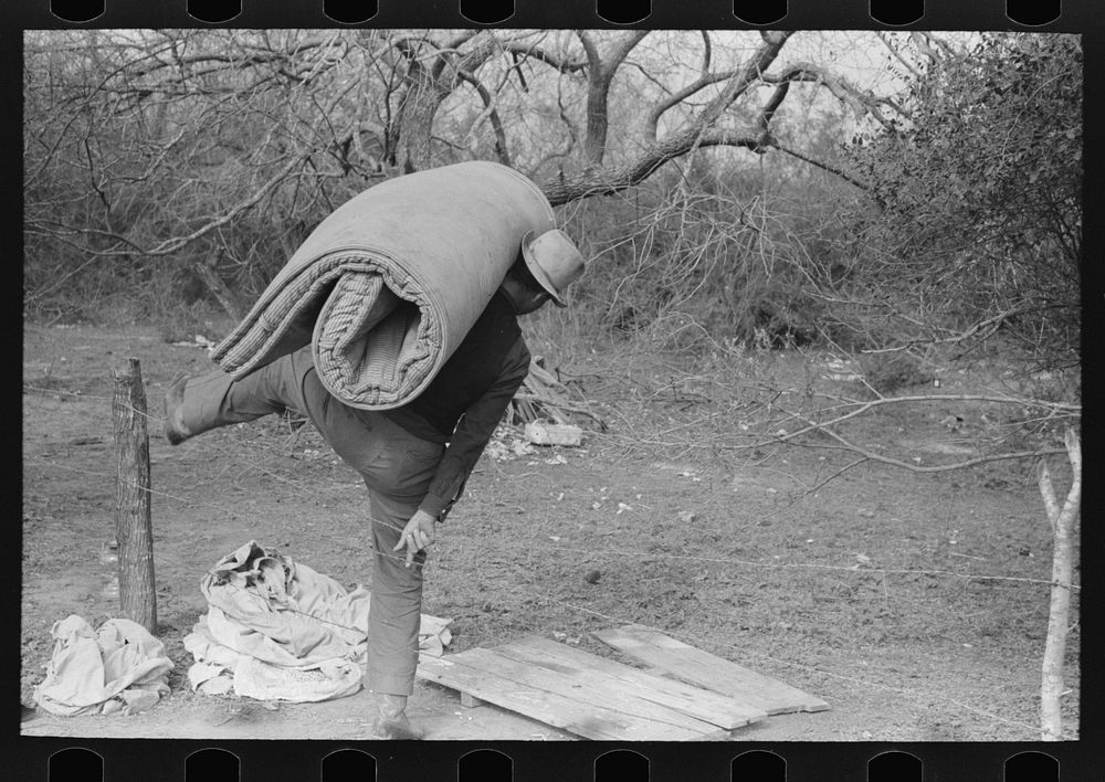 White migrant carrying mattress across fence near Harlingen, Texas by Russell Lee