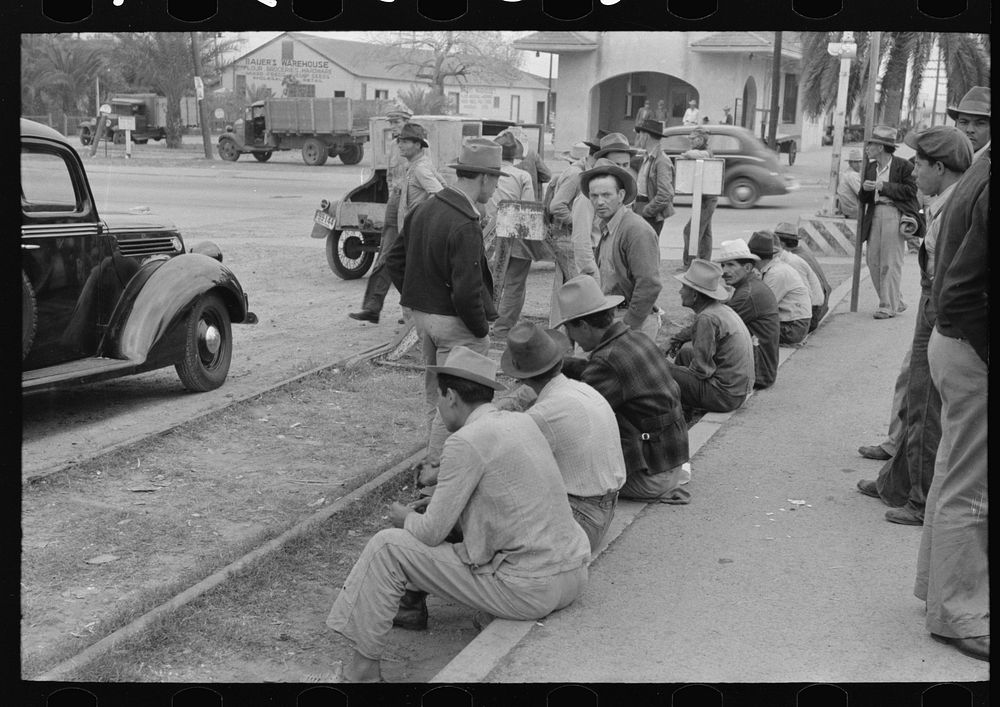 Men sitting along railroad platform waiting for work as day laborers, Raymondville, Texas by Russell Lee