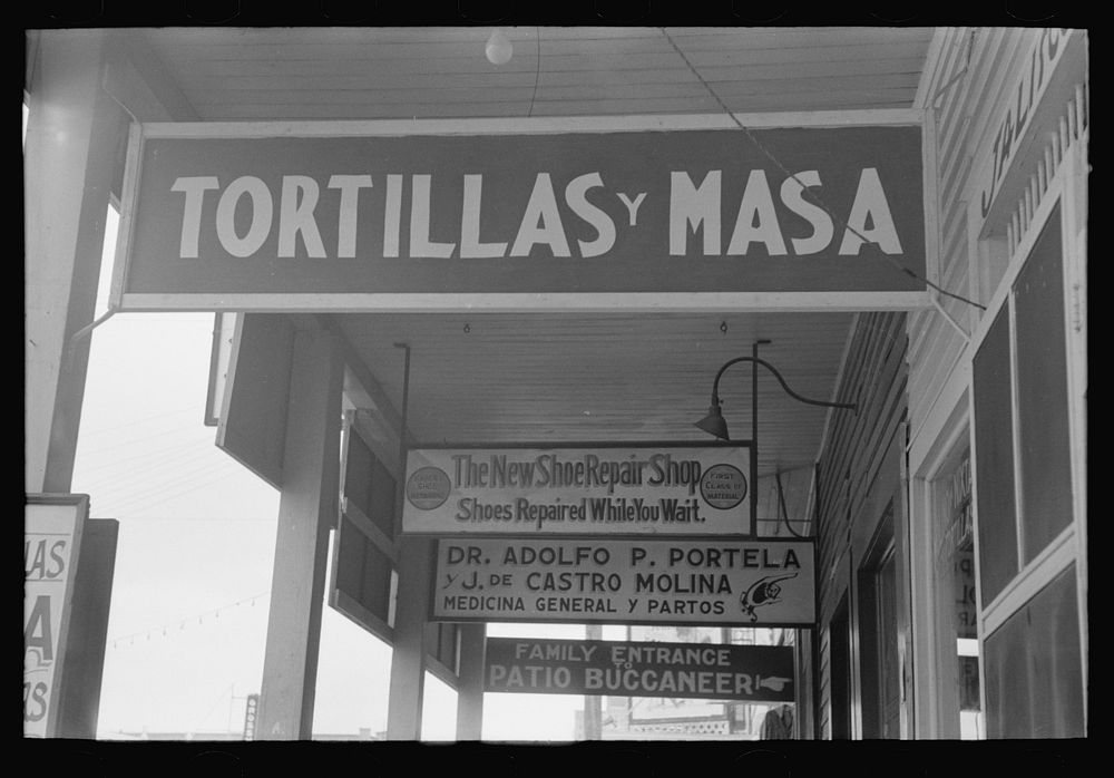 Signs hanging from balcony over sidewalk in Mexican district, Corpus Christi, Texas by Russell Lee