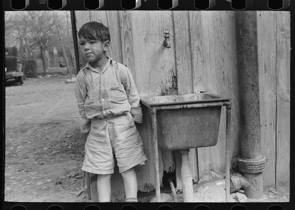 Mexican boy in front of community water hydrant and sink, San Antonio, Texas by Russell Lee