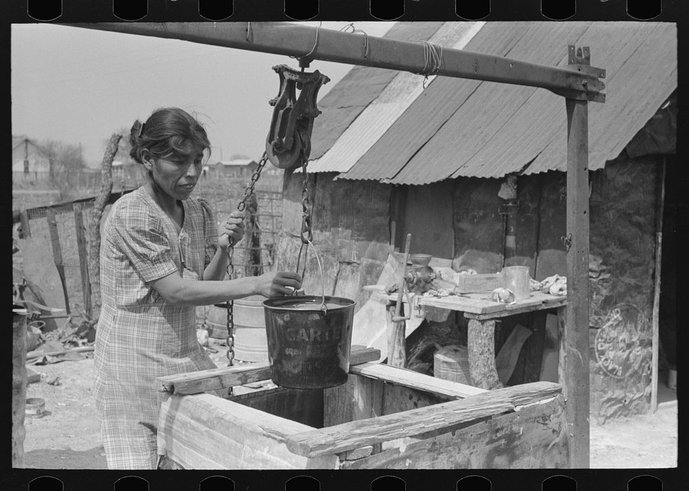 Mexican woman drawing a bucket of water from backyard well, San Antonio, Texas by Russell Lee