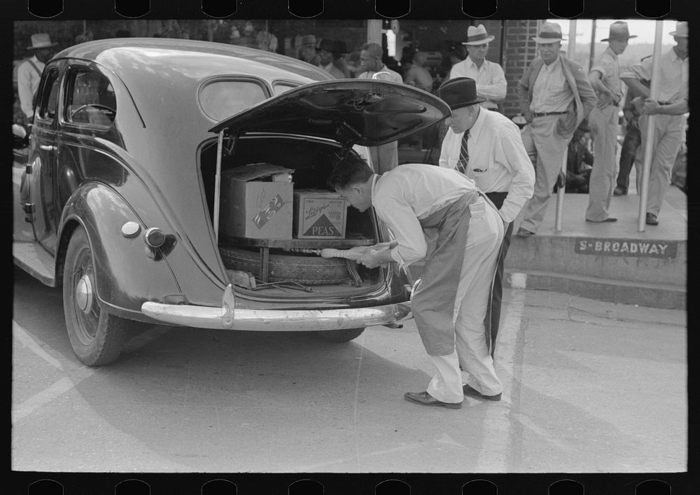 Grocery clerk putting broom and other supplies in back of automobile, Saturday afternoon, San Augustine, Texas by Russell Lee