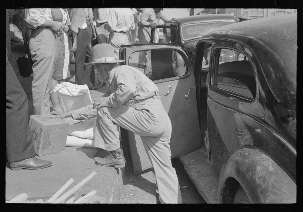 [Untitled photo, possibly related to: Grocery clerk putting broom and other supplies in back of automobile, Saturday…