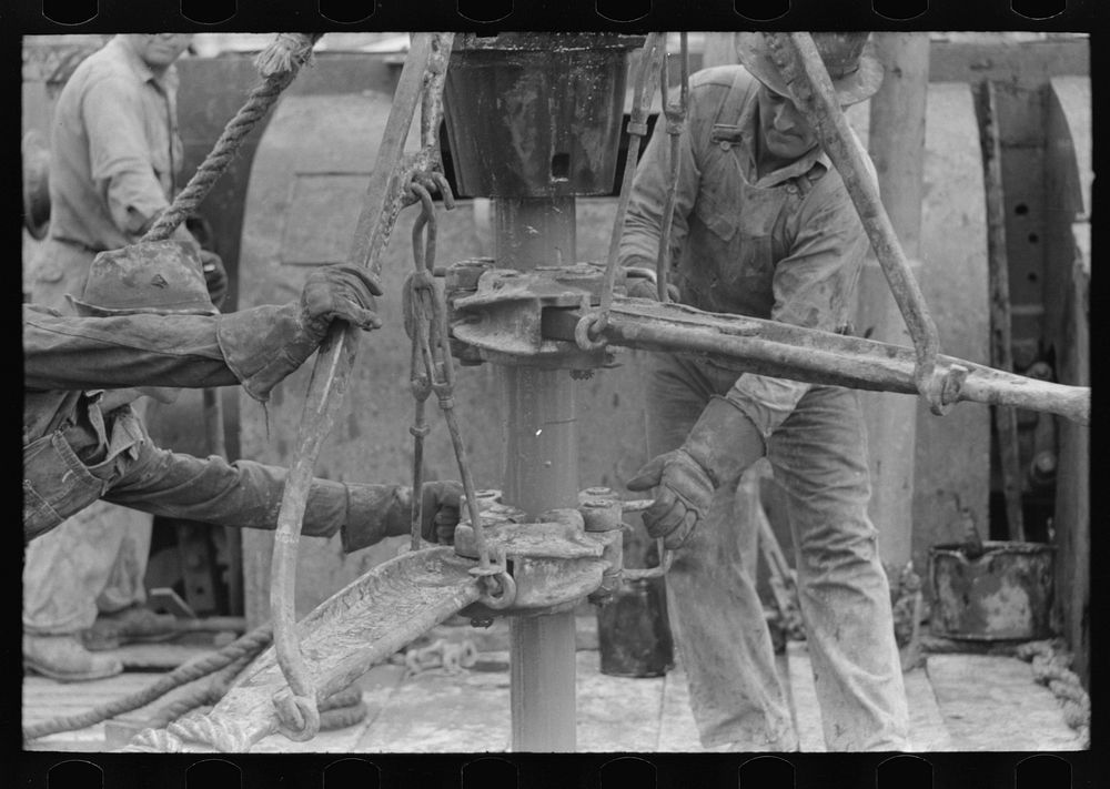 Oil field workers releasing pipe wrenches from drill pipe, oil well, Kilgore, Texas by Russell Lee