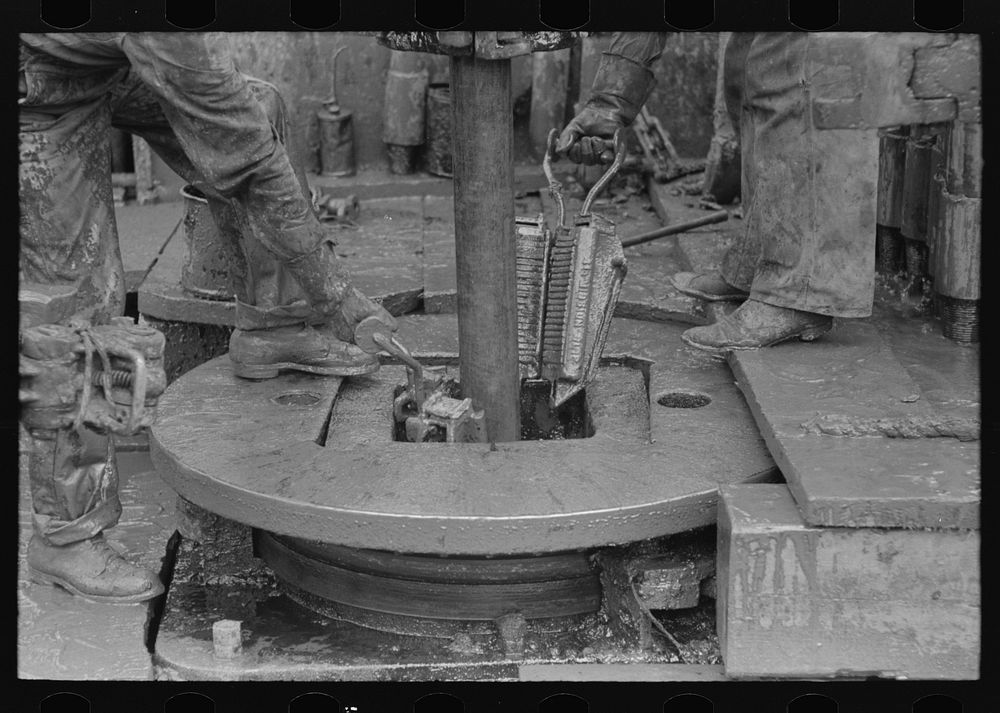 [Untitled photo, possibly related to: Removing clamps from rotary tacle before lifting out drilling pipe, oil well, Kilgore…