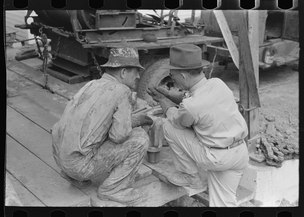 Oil field workers squatting down while talking to bit salesman, Kilgore, Texas by Russell Lee