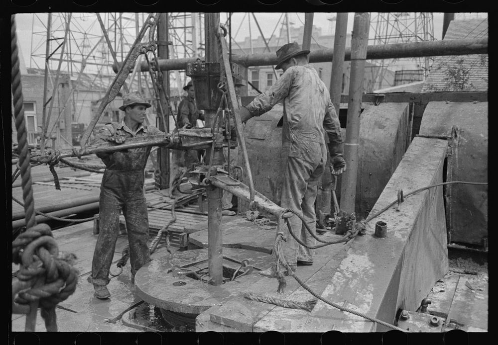 [Untitled photo, possibly related to: Oil field workers adding a length of pipe to drill stream by means of heavy pipe…